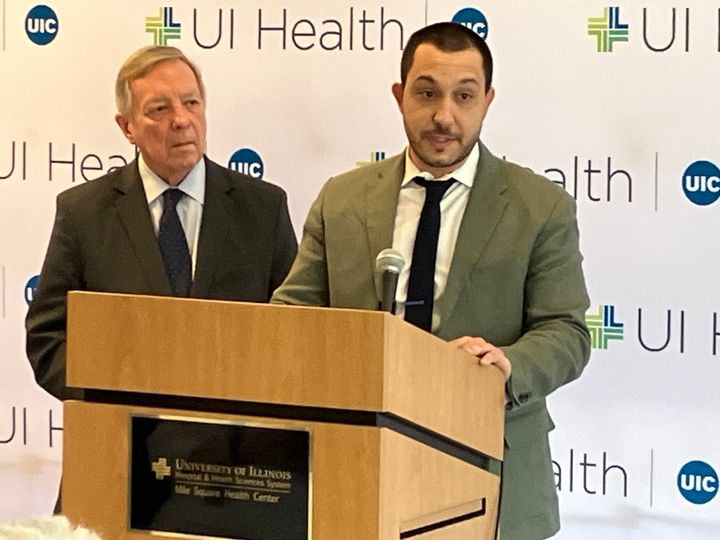 Two speakers at a podium in front of a UI Health and UIC backdrop at the press conference at Mile Square Health Center, 19 February 2026.